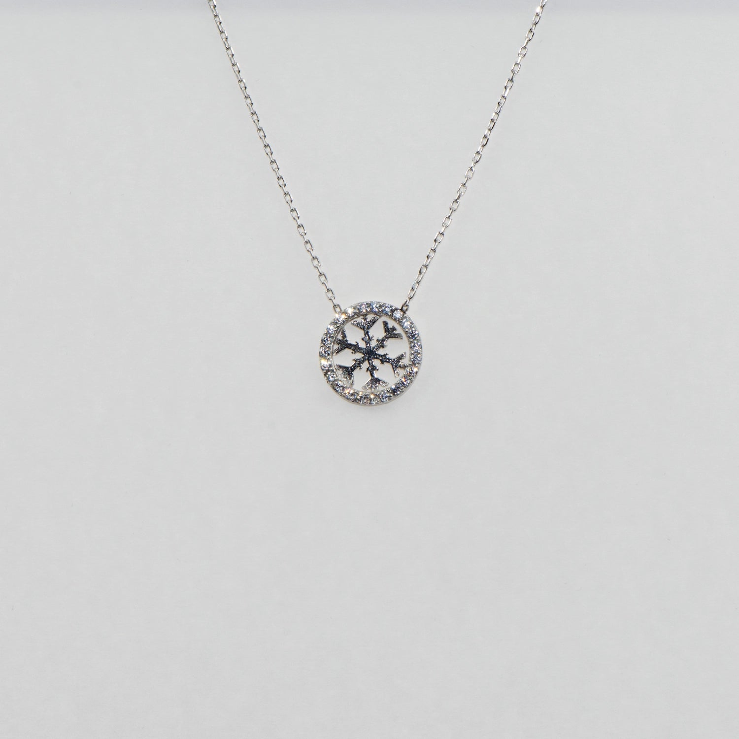 Runde 925 Silber Halskette mit Schneeflocken-Motiv im Kreis. Verziert mit funkelnden weissen Zirkonia-Steinen und rhodinierter Oberfläche.