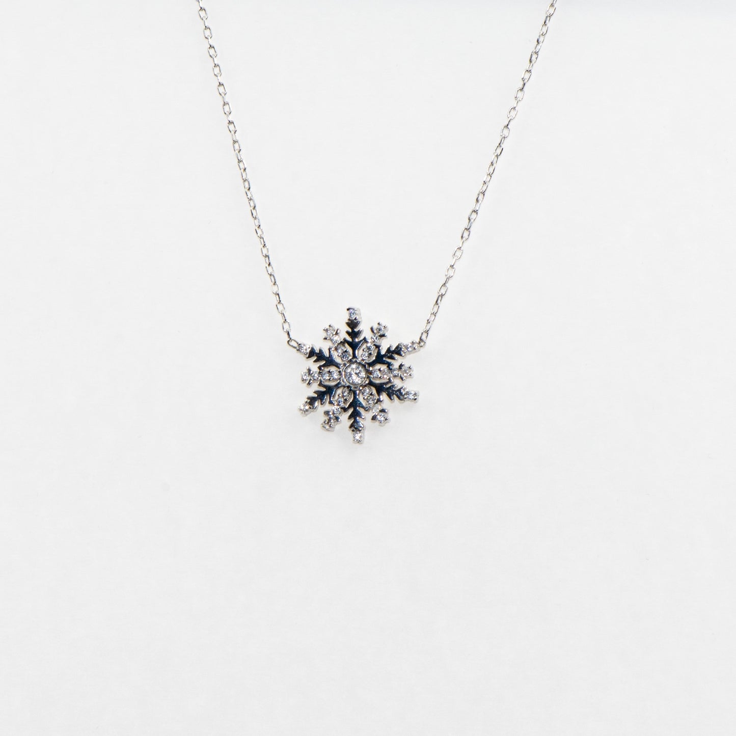 Filigrane 925 Silber Halskette mit Schneeflocken-Anhänger. Verziert mit funkelnden weissen Zirkonia-Steinen und rhodinierter Oberfläche.