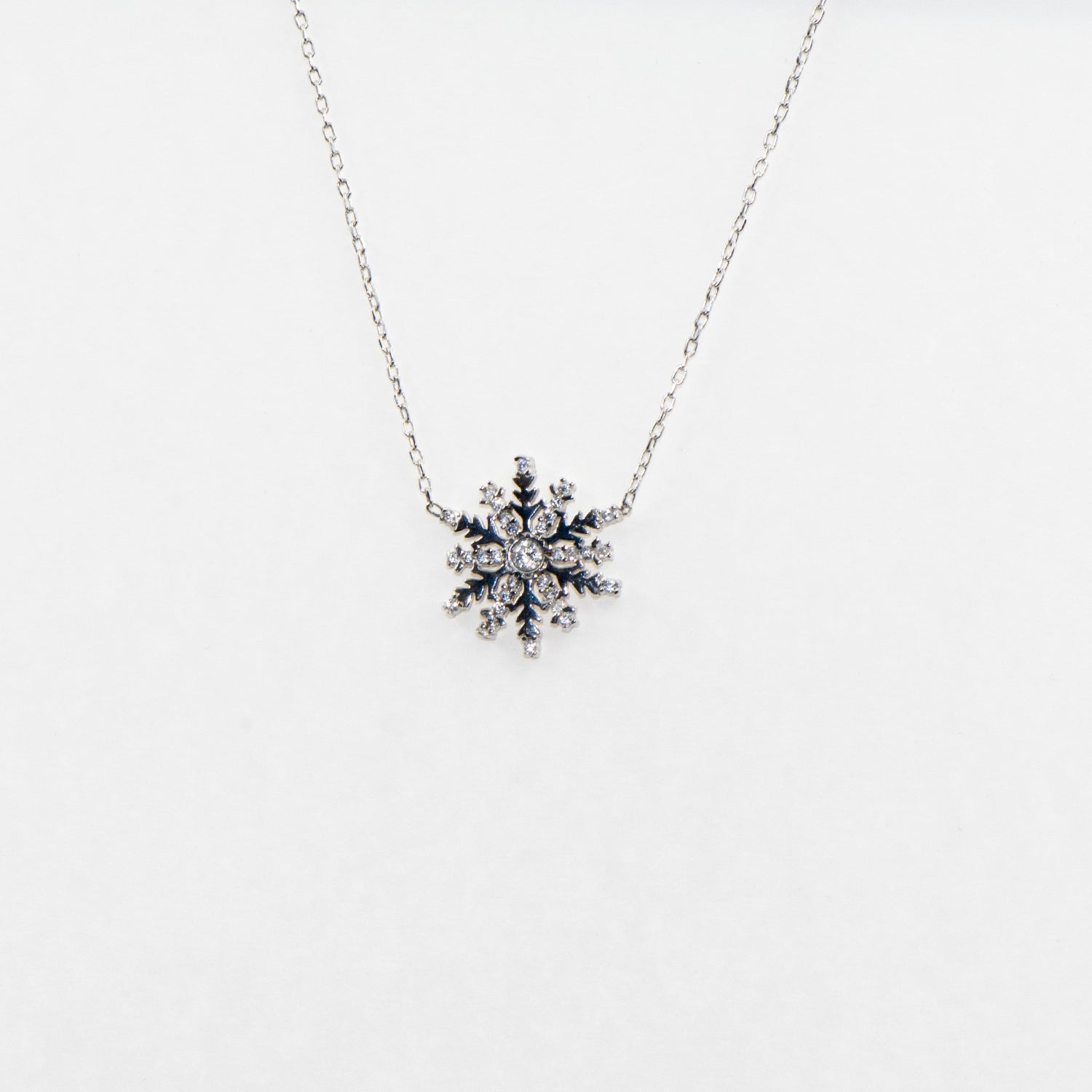 Filigrane 925 Silber Halskette mit Schneeflocken-Anhänger. Verziert mit funkelnden weissen Zirkonia-Steinen und rhodinierter Oberfläche.